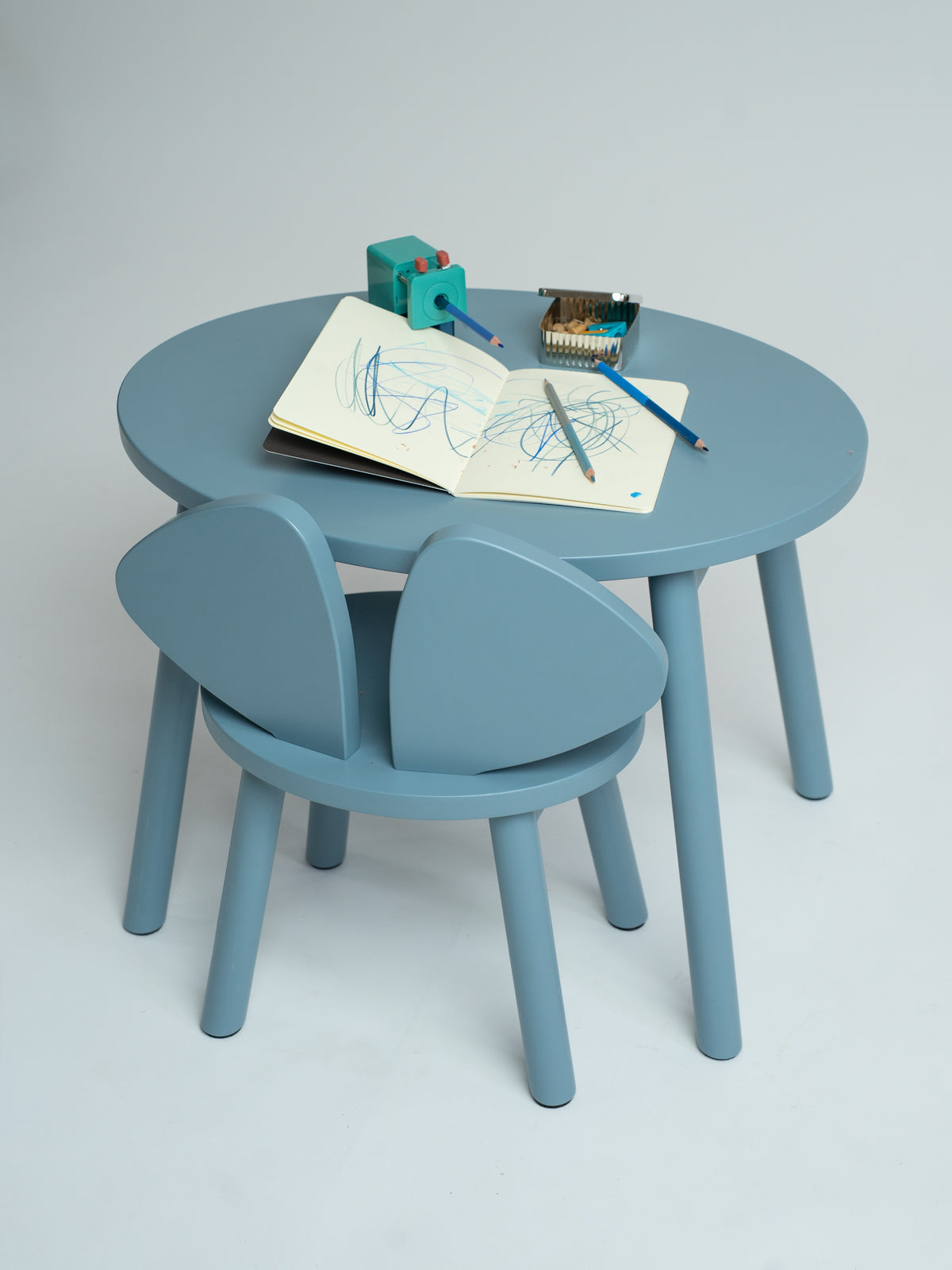 A light blue children's table and chair set with a round table and two matching chairs, styled with drawing accessories on a neutral studio background.
