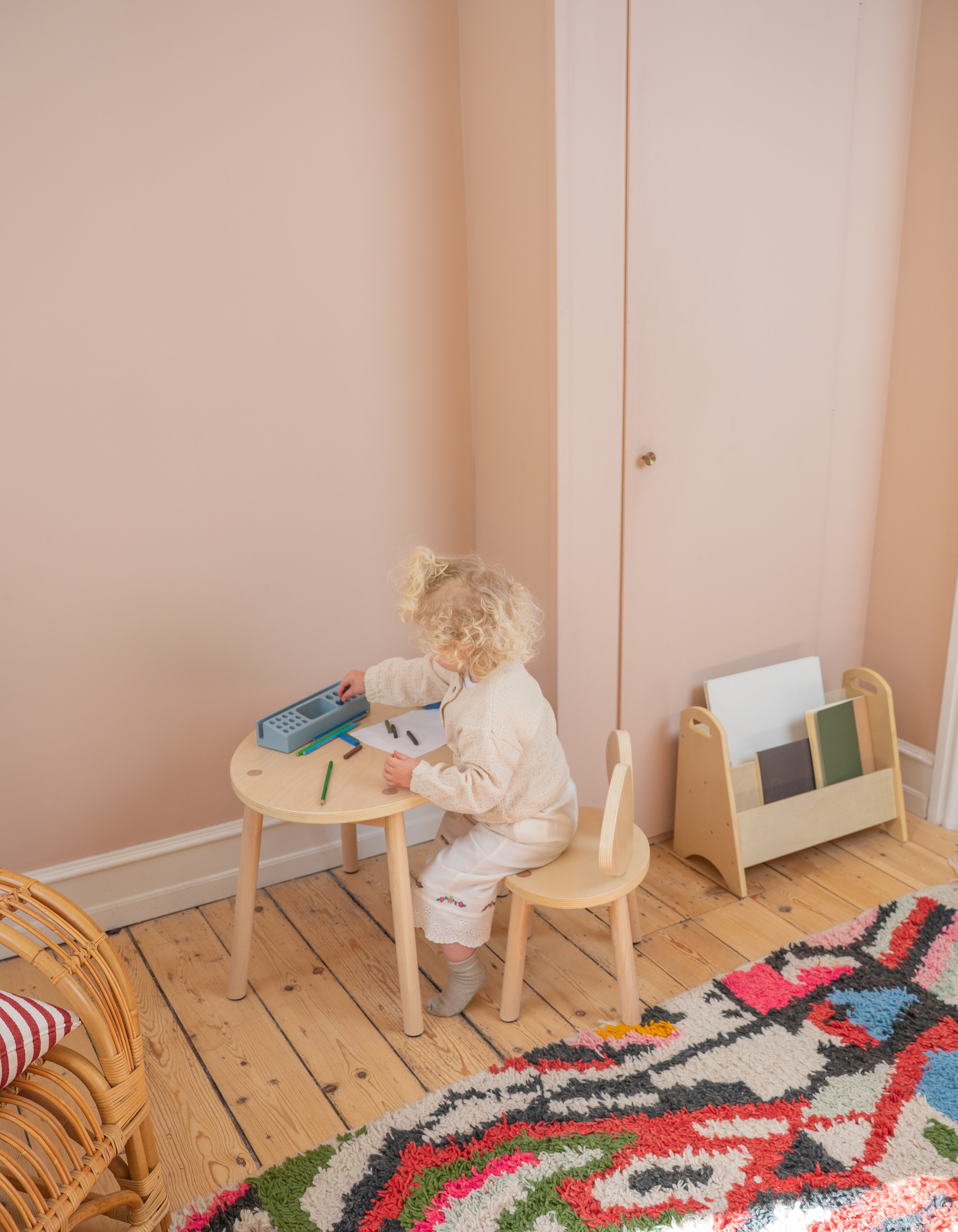 Child sitting at a small table with a colorful rug on the floor