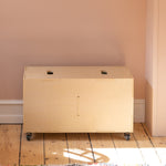 Beige storage cabinet on wheels against a light pink wall with a colorful rug on the floor.