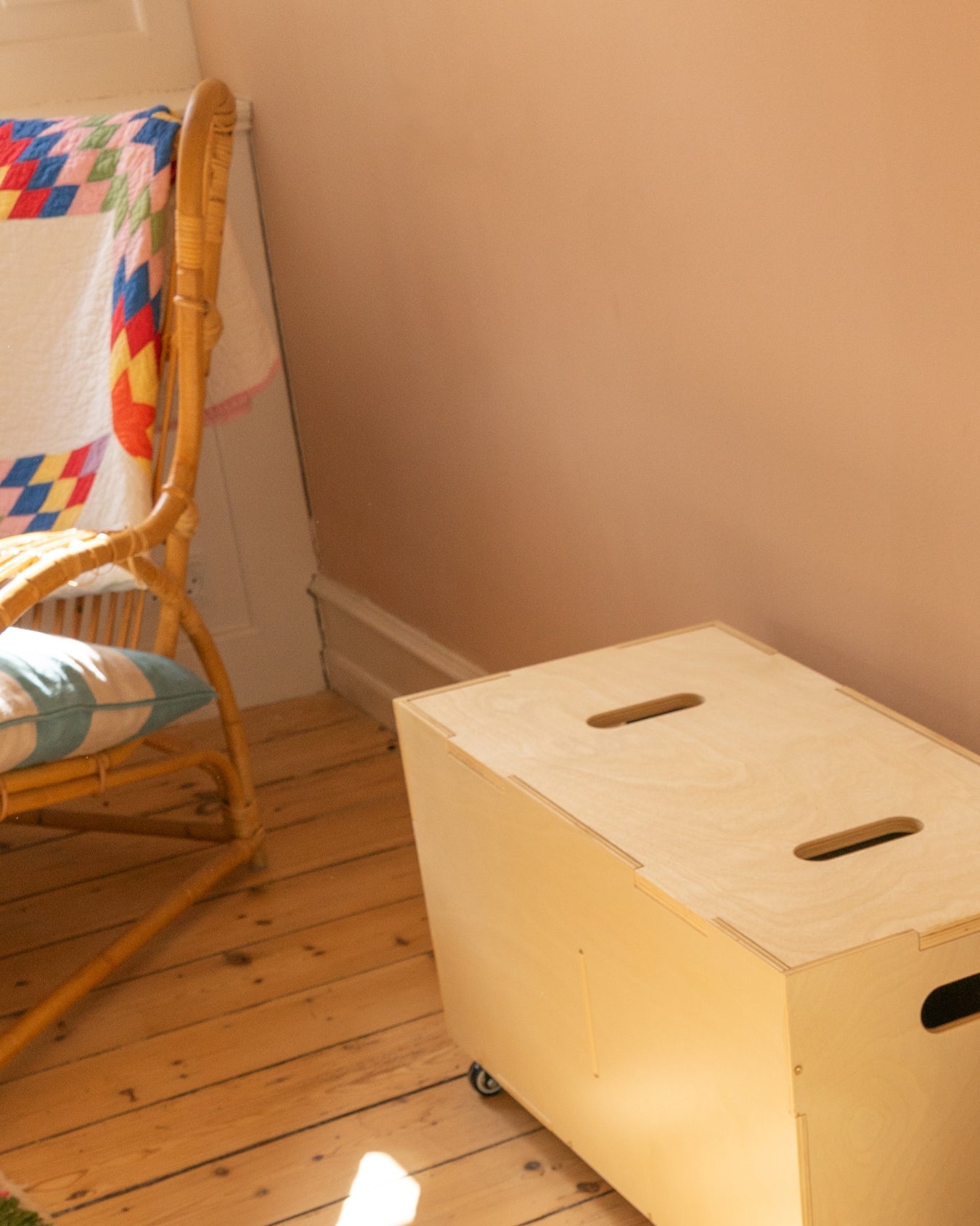 Birch Nofred Cube Long storage bench on wheels, viewed from above beside a wicker chair on a wooden floor.