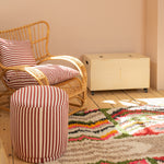 Wicker chair with striped cushions and a matching ottoman on a colorful rug.