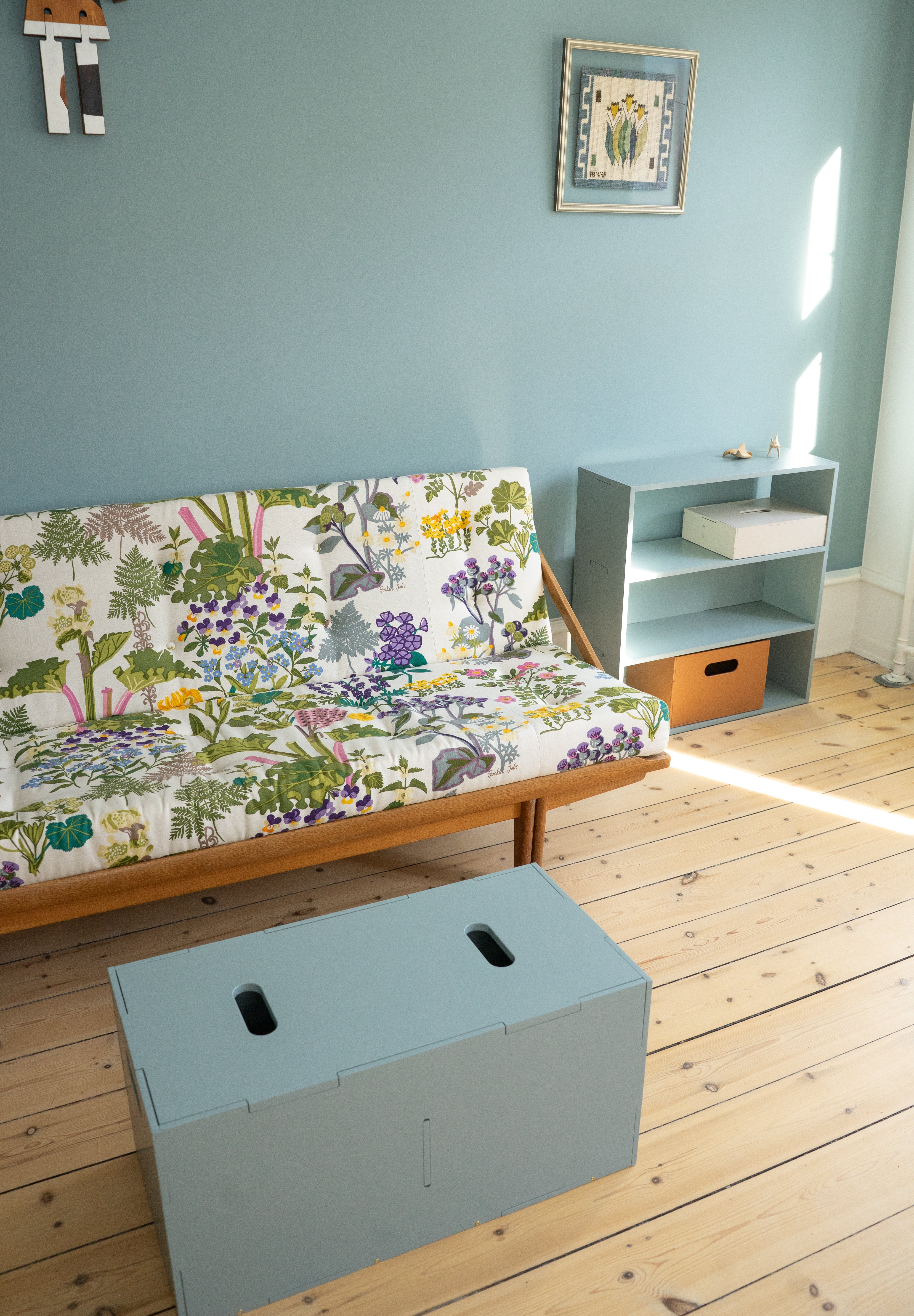Room with a colorful futon, small table, and storage box on wooden floor.