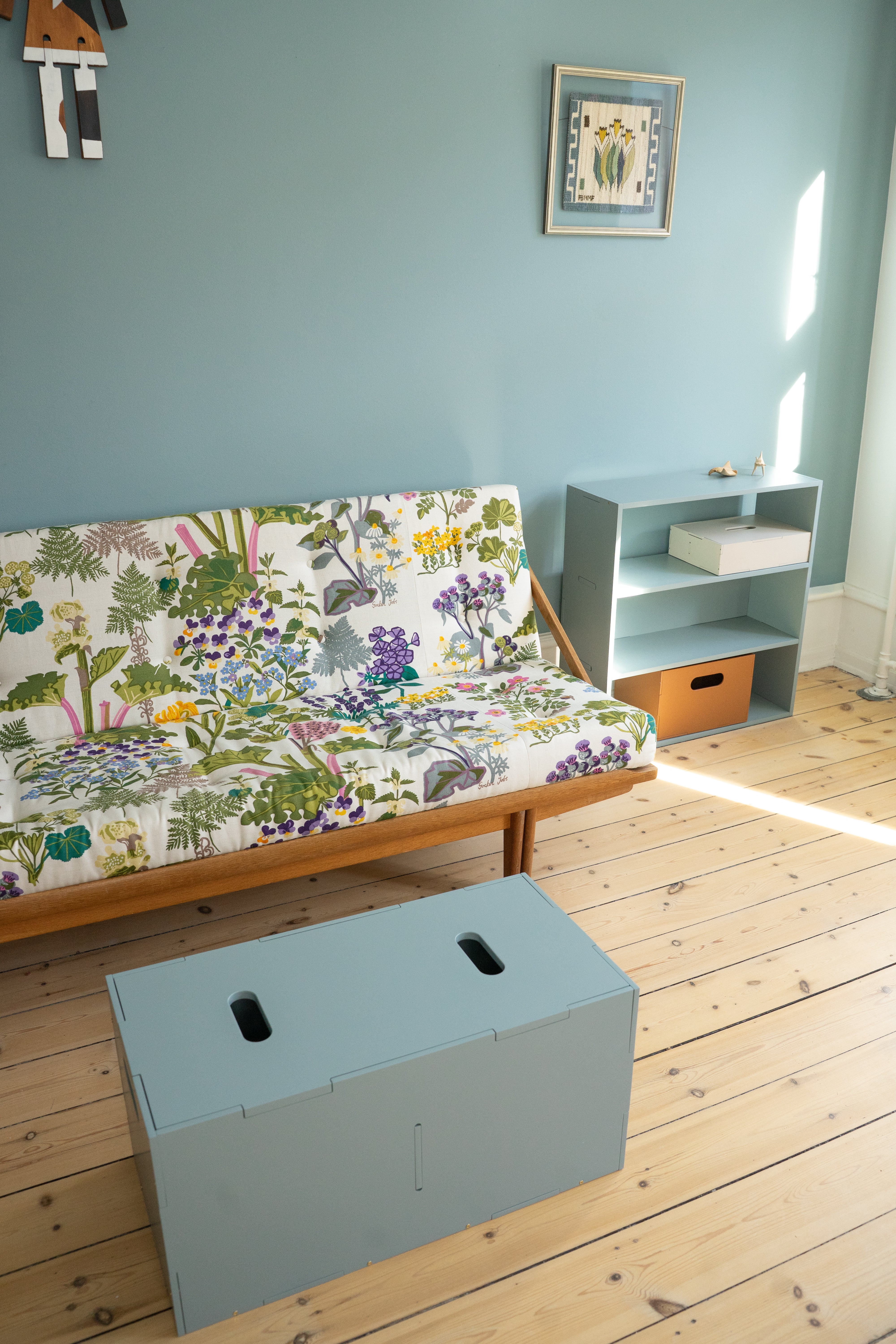 Room with a colorful futon, small table, and storage box on wooden floor.