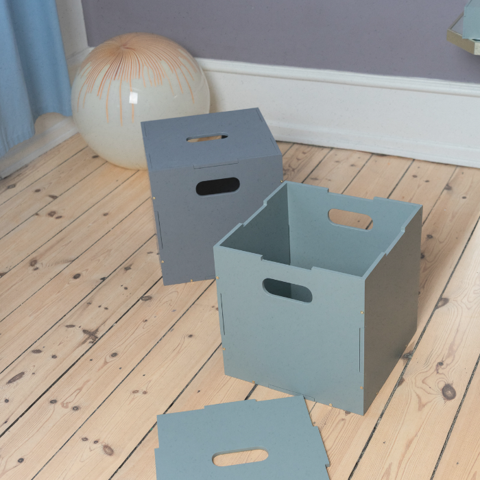 Three gray storage boxes on a wooden floor with a blue wall and decorative elements in the background.