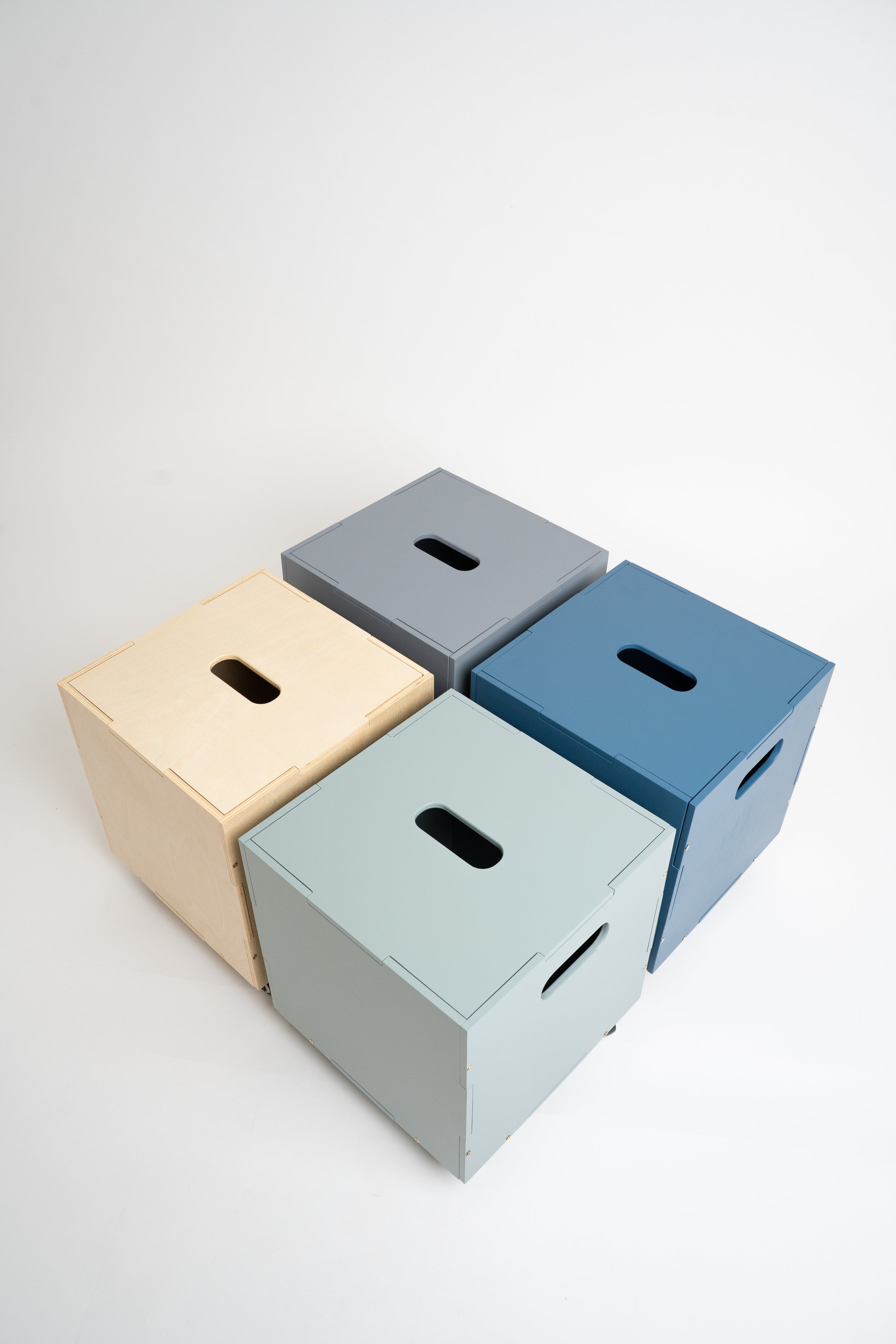 Four minimalist cube storage boxes with handle cutouts, shown in beige, gray, blue, and light green on a clean white background.