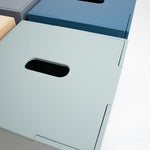 Three minimalist metal storage boxes with integrated handles, shown in gray, blue, and pale sage green on a clean white background.