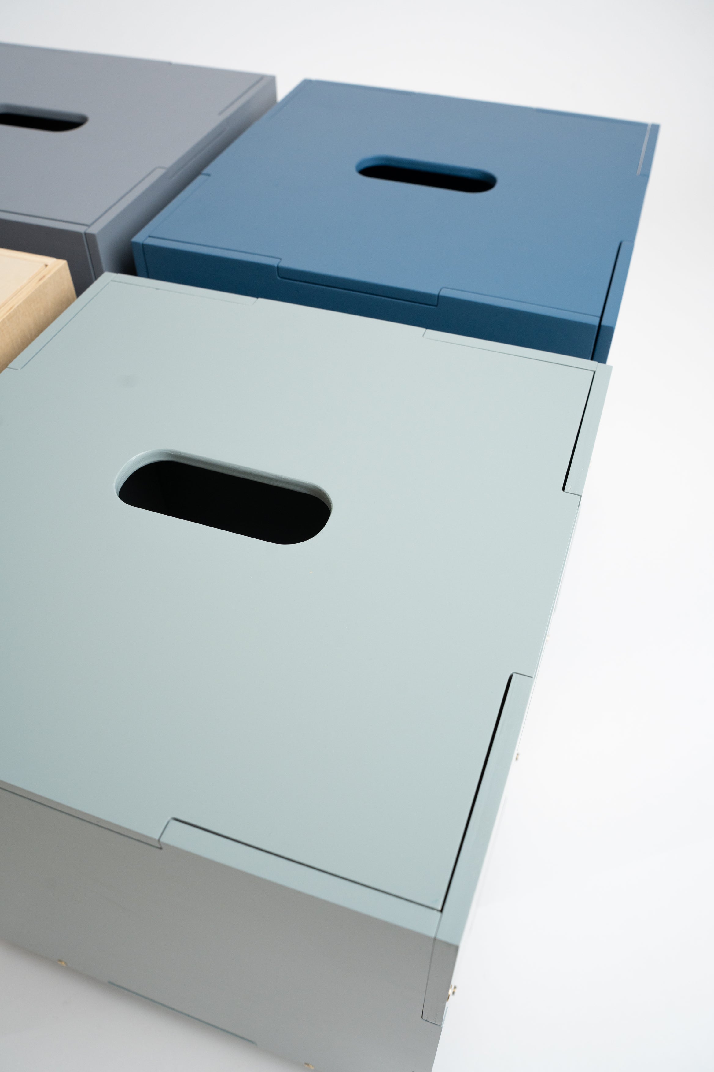 Three minimalist metal storage boxes with integrated handles, shown in gray, blue, and pale sage green on a clean white background.