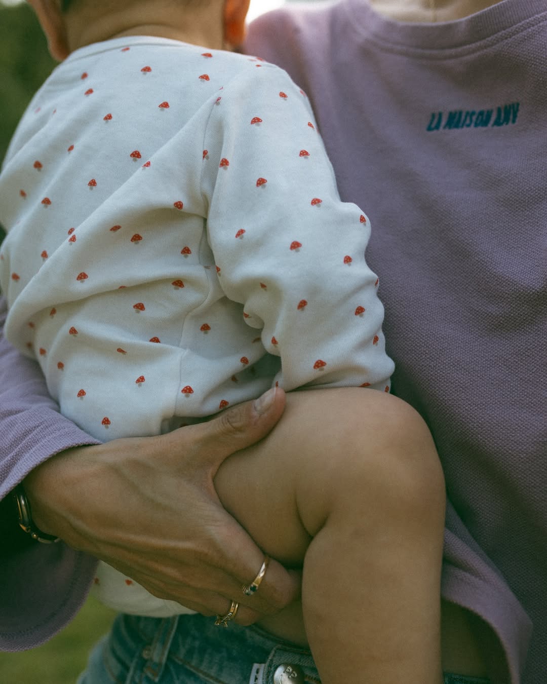 Person holding a child wearing a white outfit with red polka dots.
