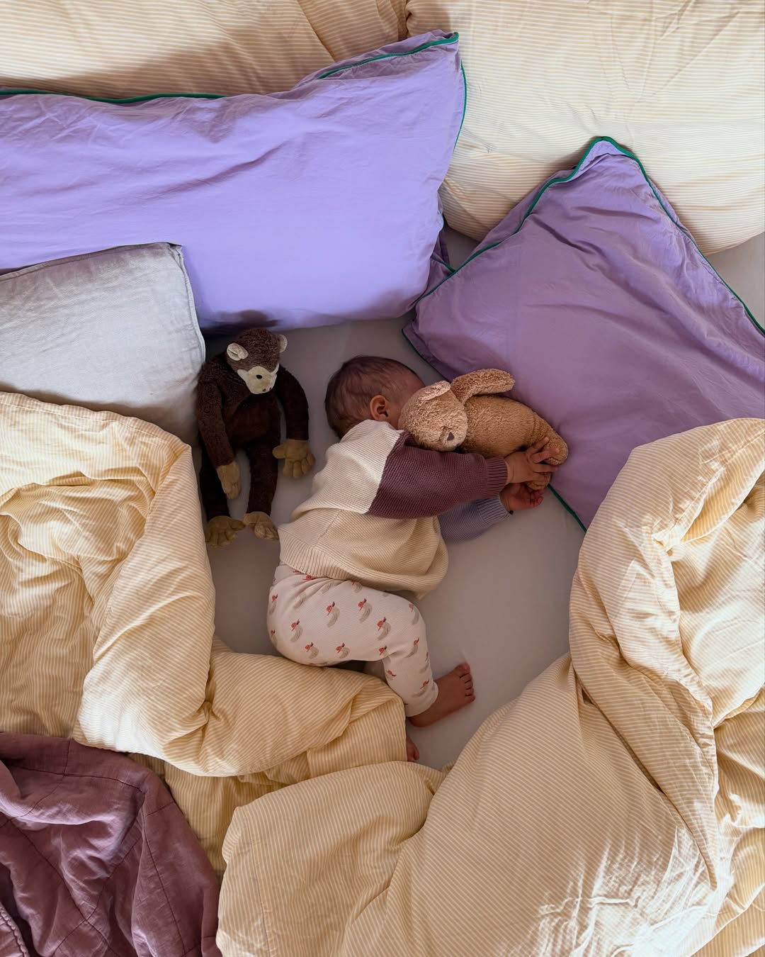Child playing with stuffed animals on a bed with pillows and blankets.