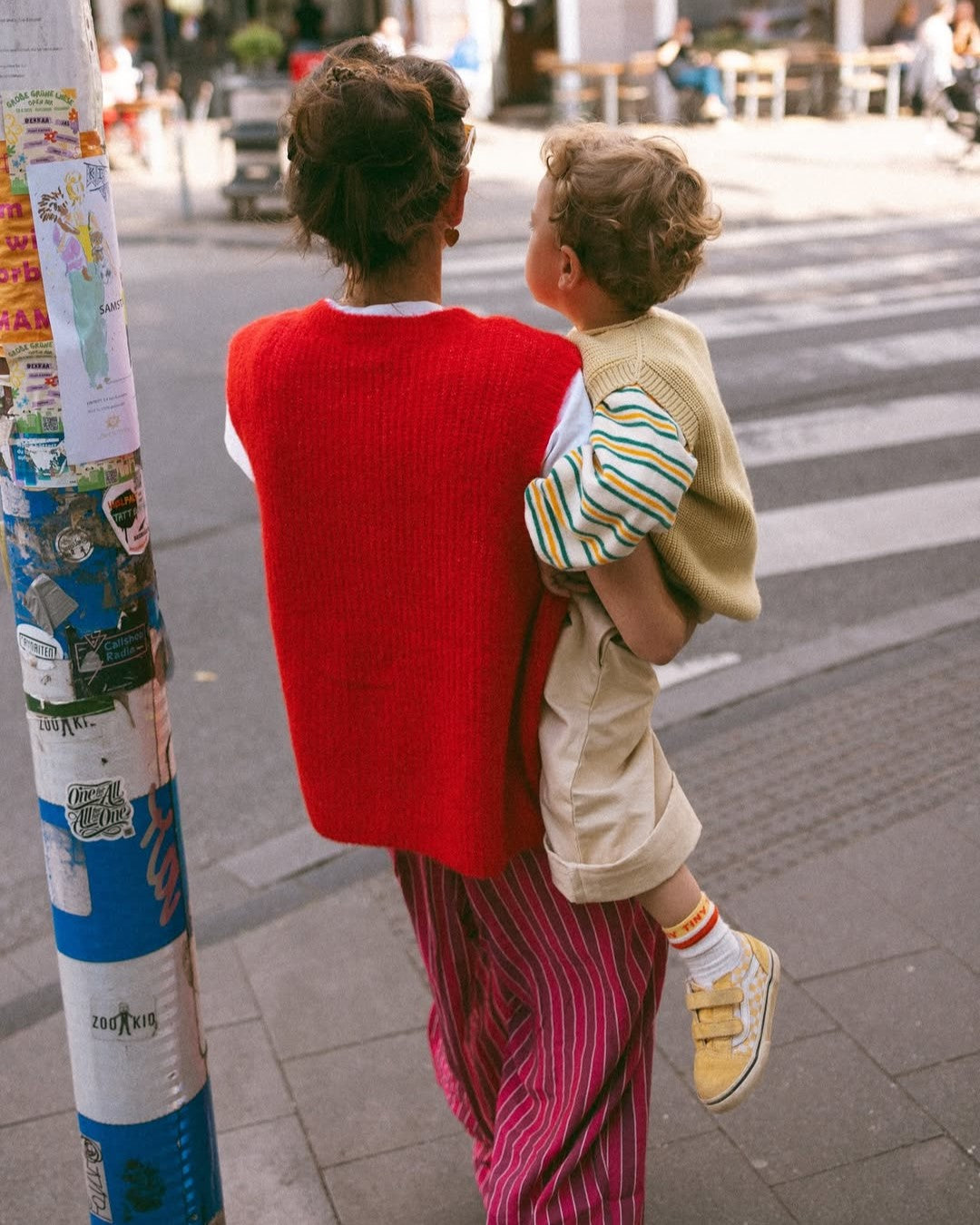 Person holding a child on a city street with posters and a crosswalk in the background