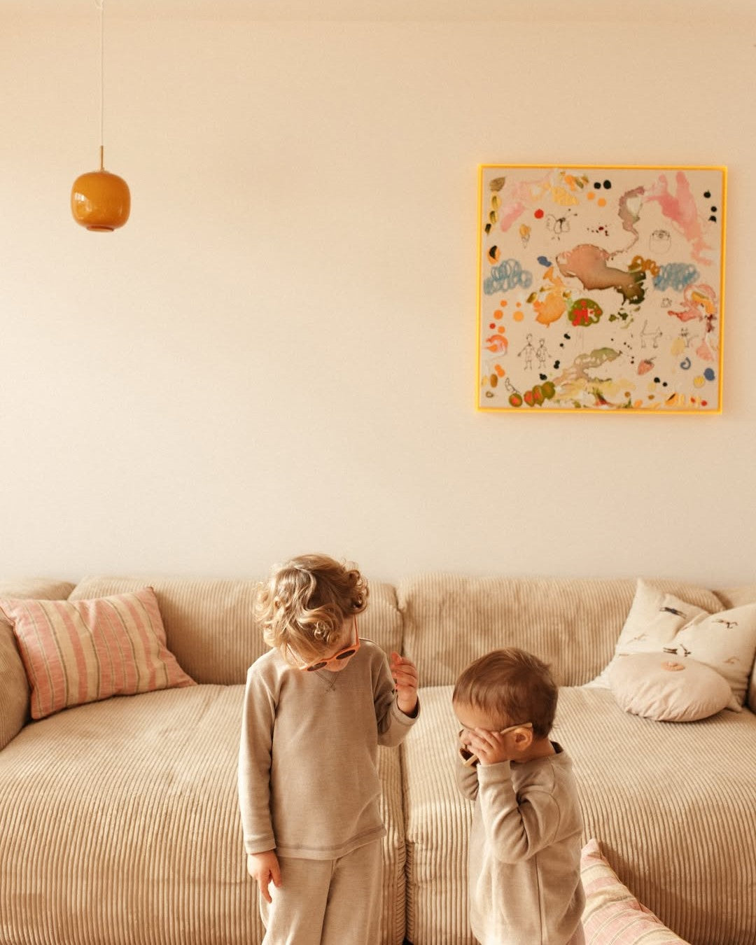 Two children standing on a couch in a room with a colorful wall art piece.