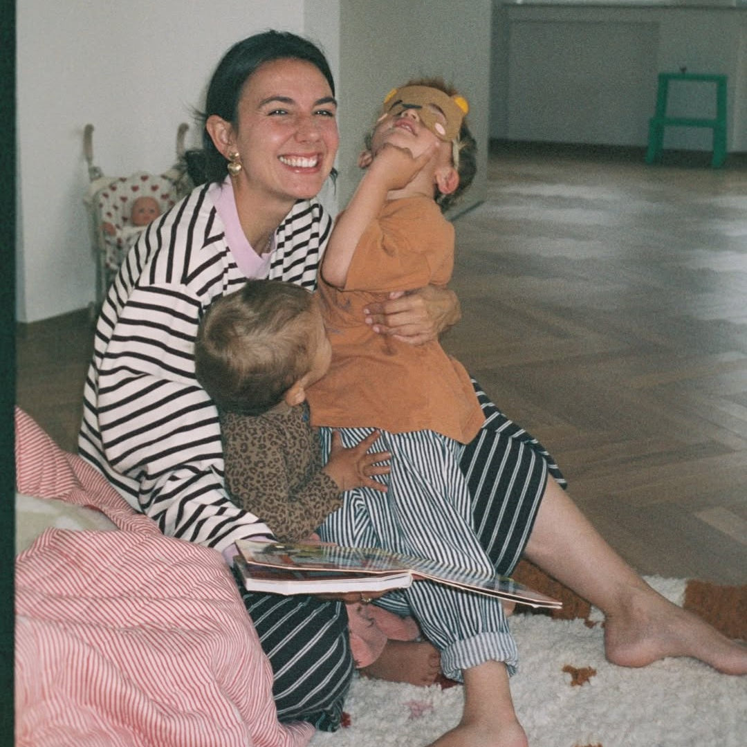Woman and child sitting on a bed reading a book together in a cozy room.