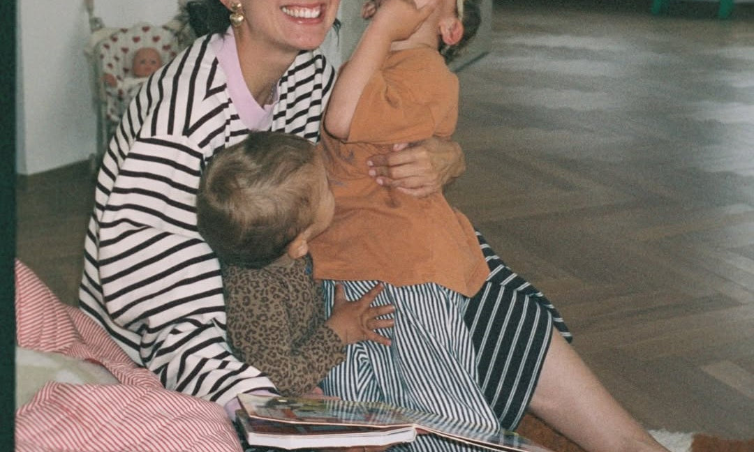 Woman and child sitting on a bed reading a book together in a cozy room.