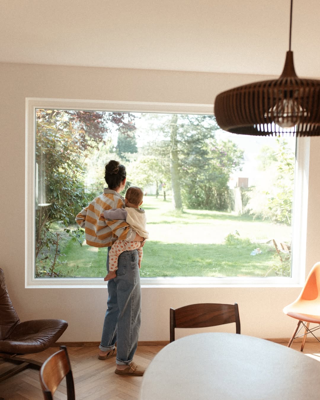 Woman holding a child by a large window with a view of greenery