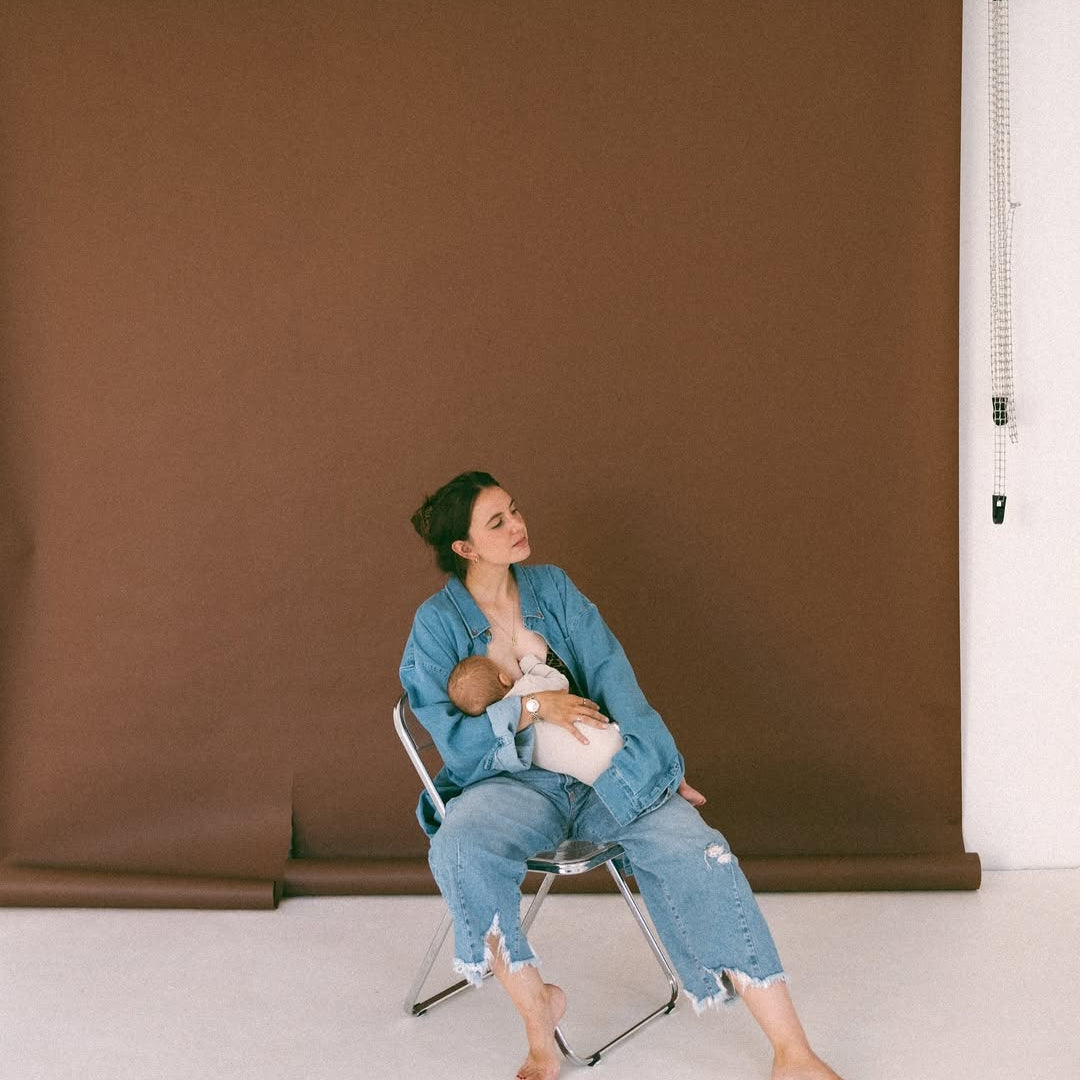 Woman sitting on a chair against a brown backdrop, holding a baby.