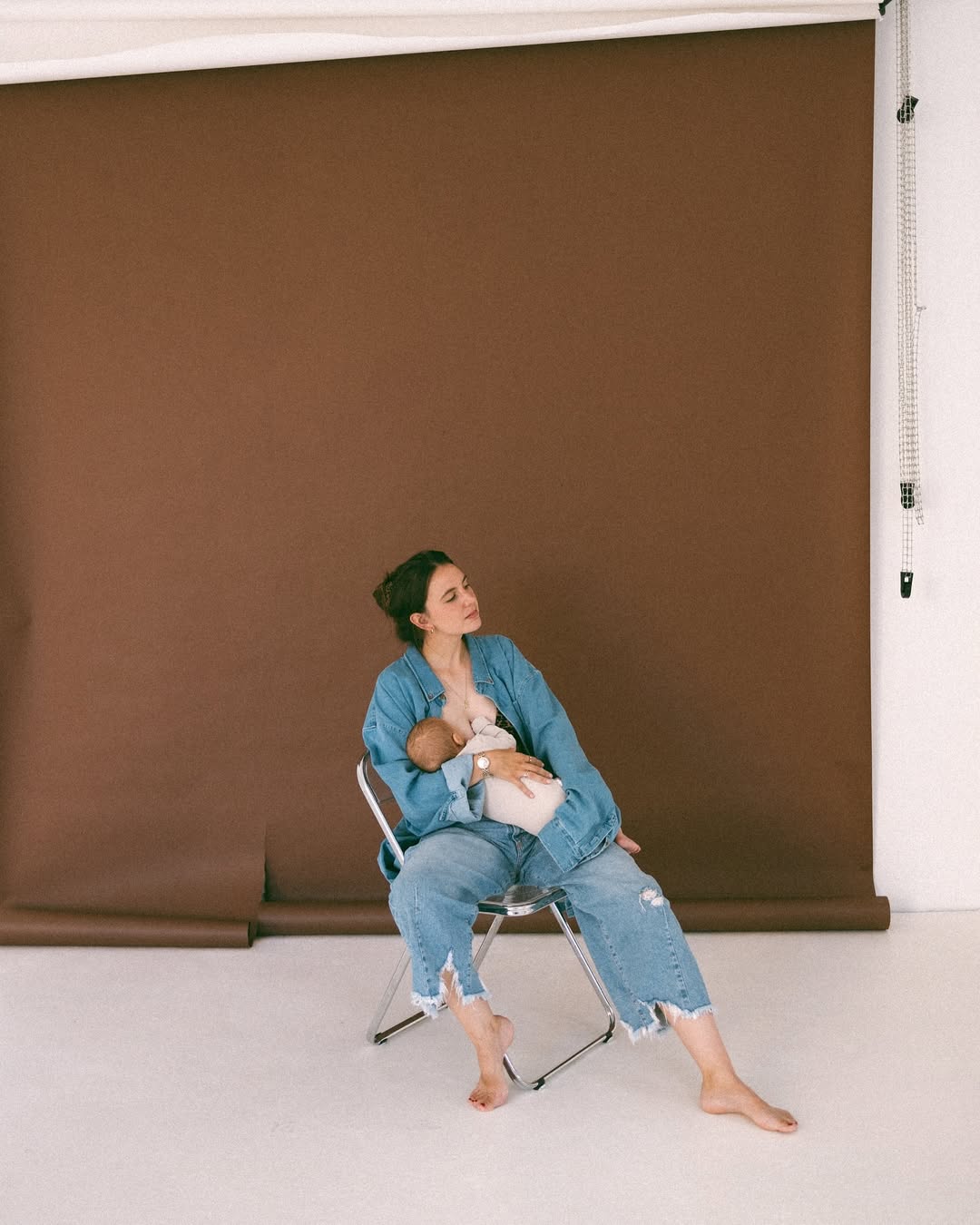 Woman sitting on a chair against a brown backdrop, holding a baby.