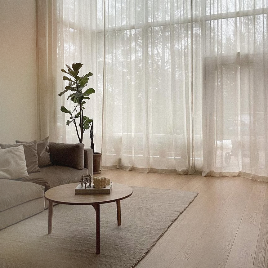 Living room with a sofa, coffee table, and large windows with sheer curtains.