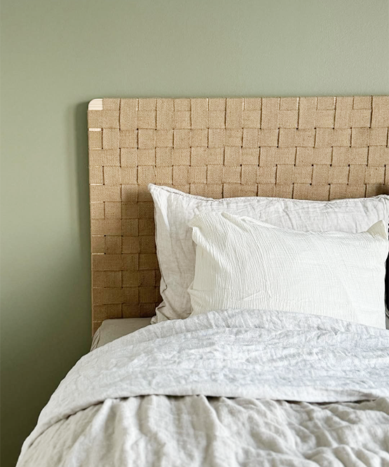 Bed with woven headboard and white bedding against a green wall