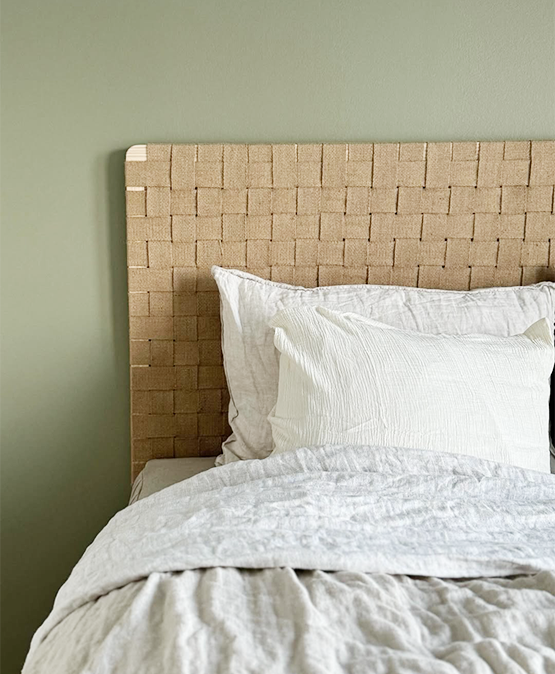 Bed with woven headboard and white bedding against a green wall