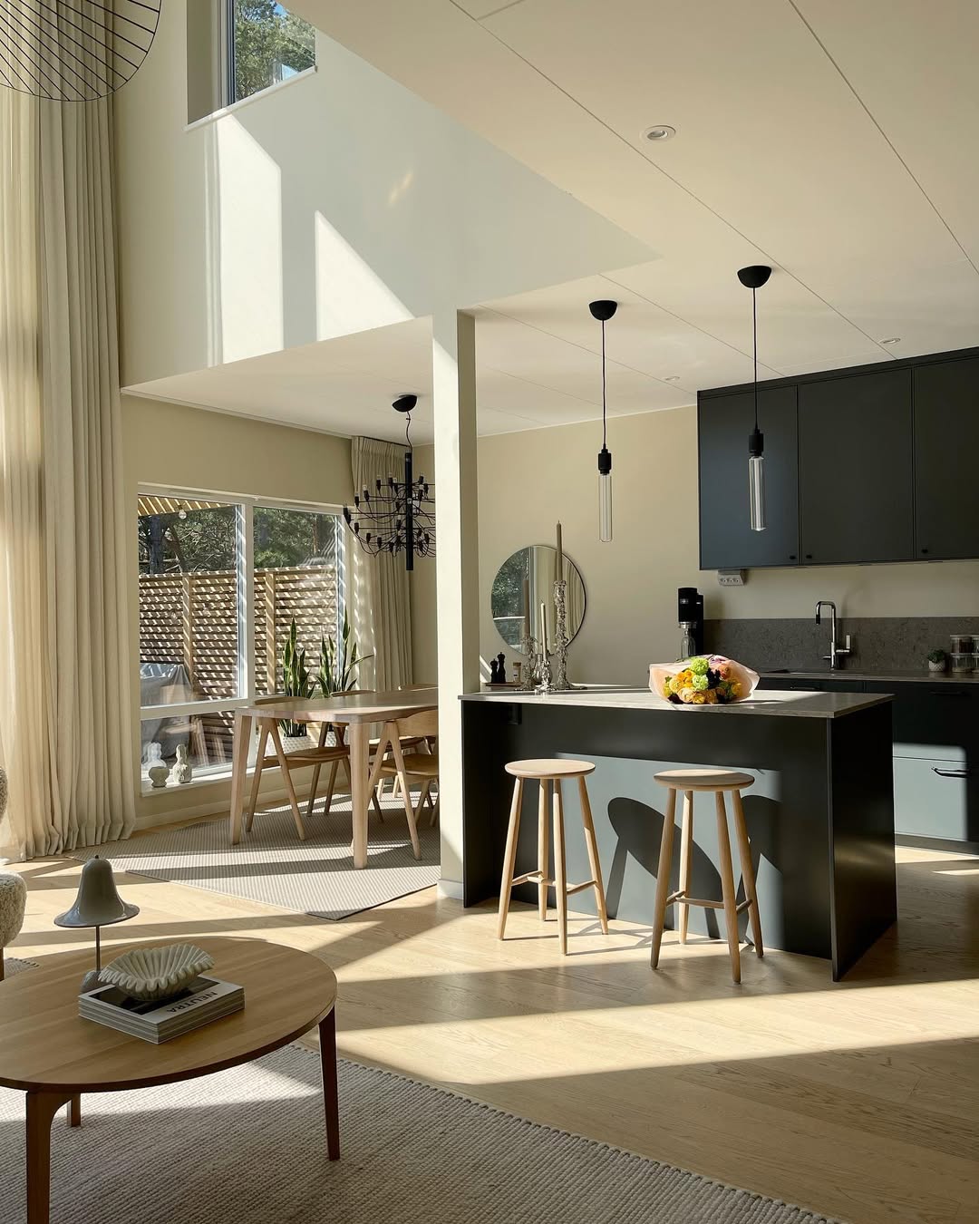 Modern kitchen with black island, wooden dining table, and living room in the background.