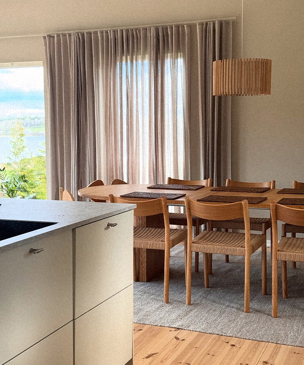 Modern kitchen with wooden dining table and chairs, large window with curtains, and lamp.