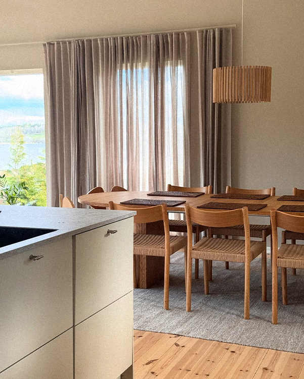 Modern kitchen with wooden dining table and chairs, large window with curtains, and lamp.
