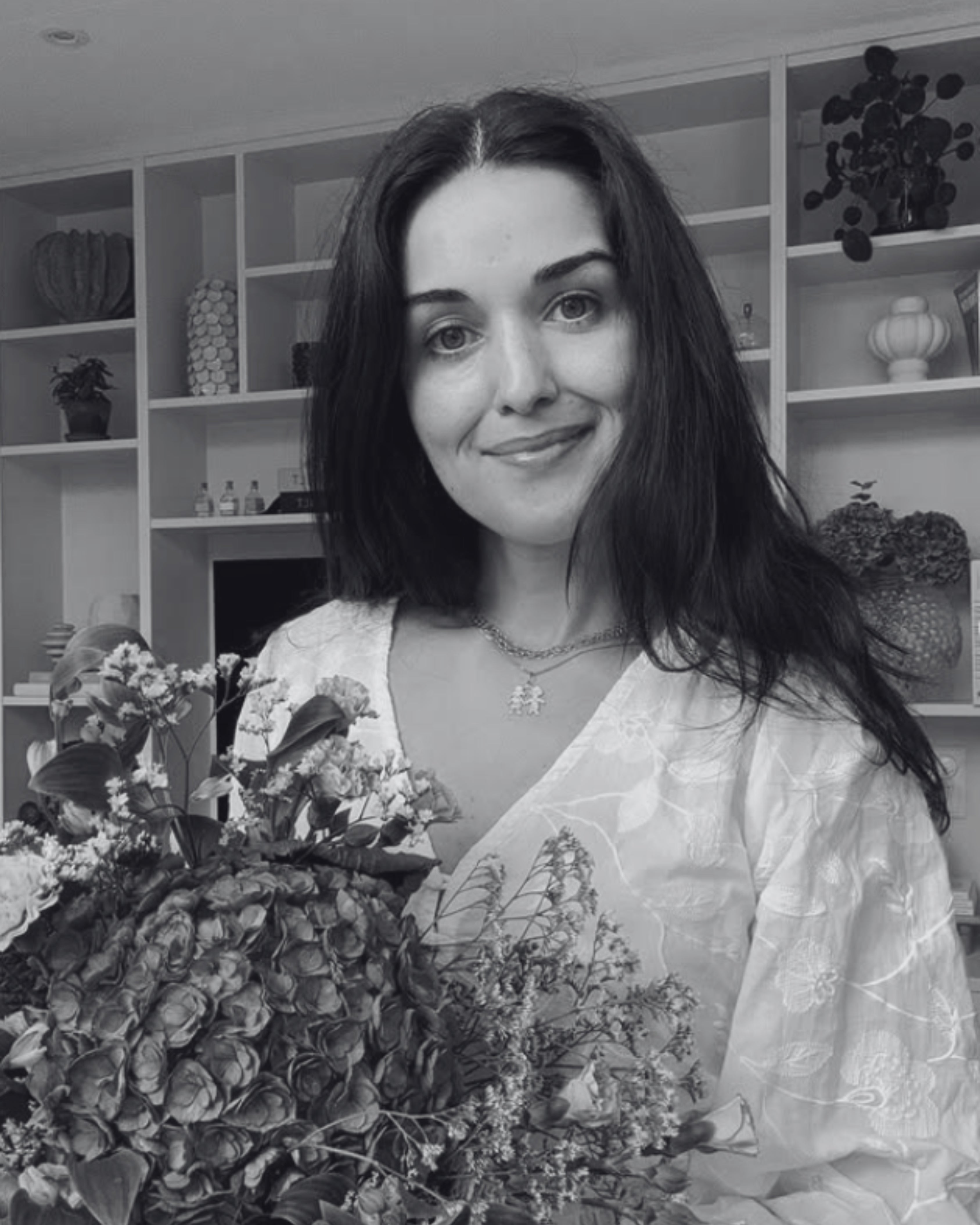 Woman holding a large bouquet of flowers indoors with shelves in the background