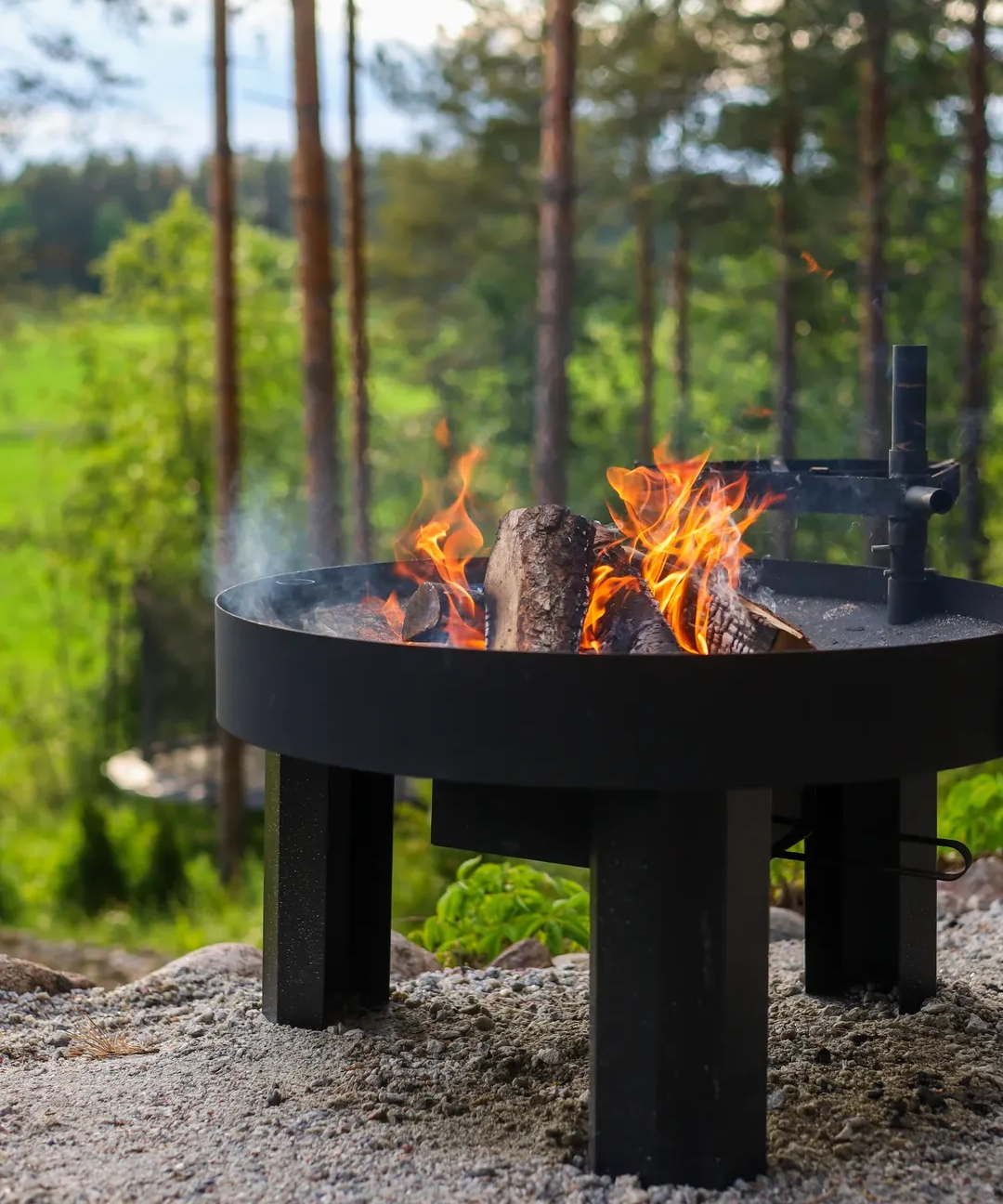 Black fire pit with flames in a forest setting