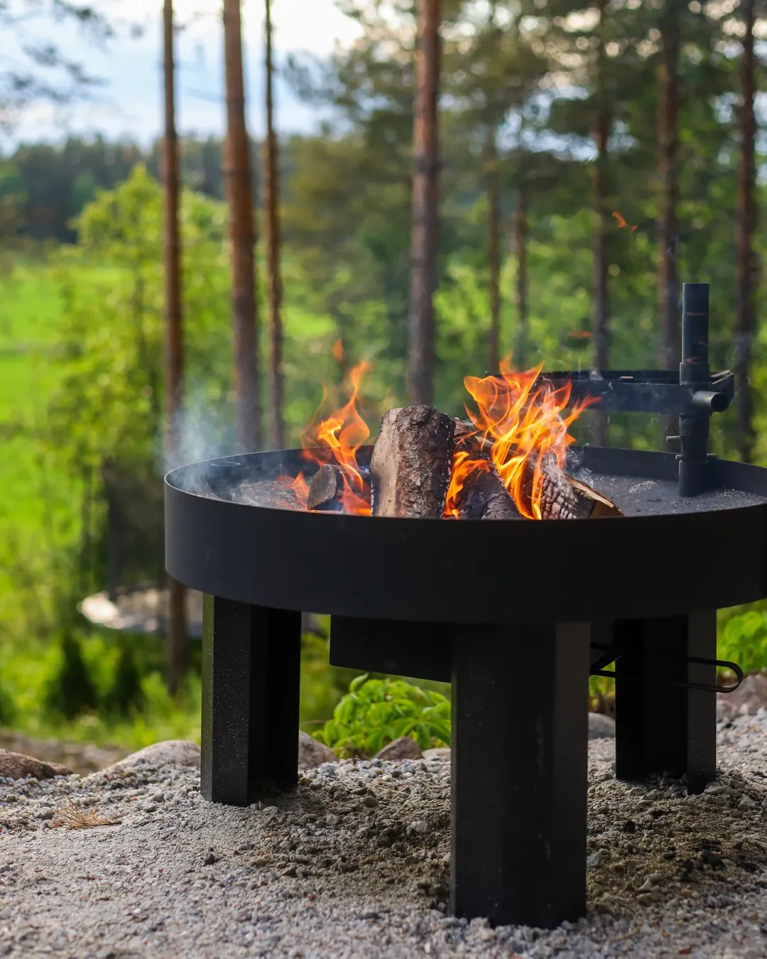 Black fire pit with flames in a forest setting