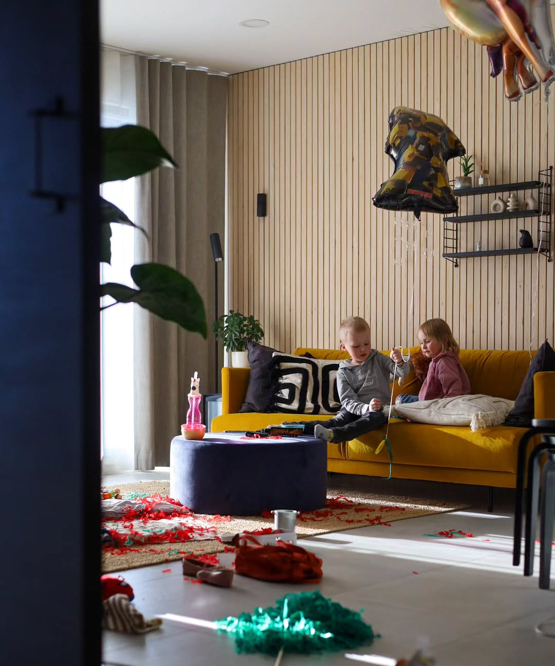 Children playing on a yellow couch in a modern living room with decorative items.