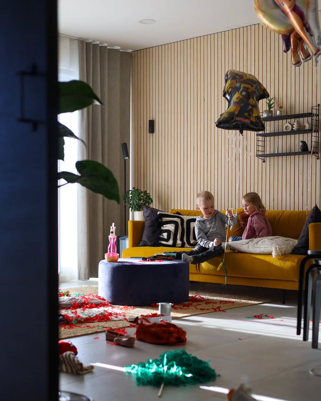 Children playing on a yellow couch in a modern living room with decorative items.