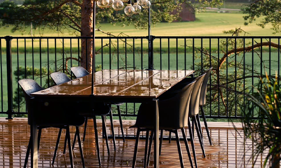 Outdoor dining area with a table and chairs on a wooden deck, surrounded by nature.