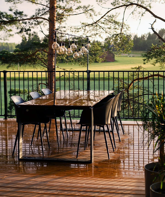 Outdoor dining area with a table and chairs on a wooden deck, surrounded by nature.