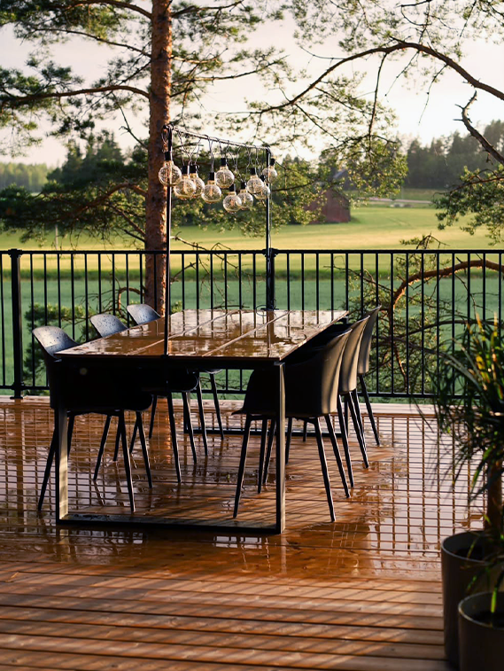 Outdoor dining area with a table and chairs on a wooden deck, surrounded by nature.