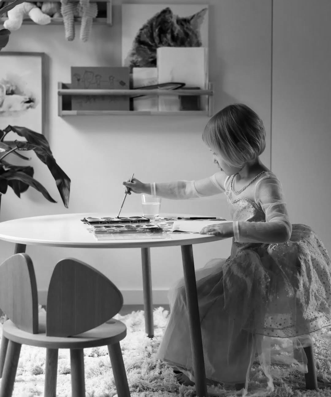 Black and white photo of a child sitting at a small table with art supplies.