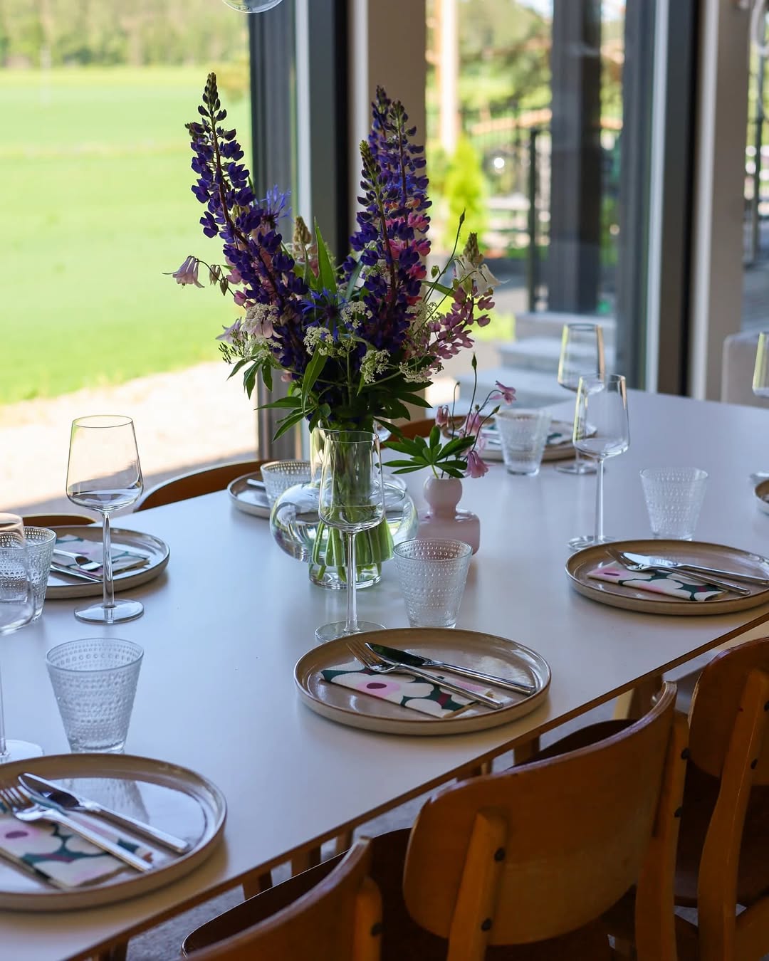 Dining table set with floral centerpiece, glasses, and cutlery in a bright room.