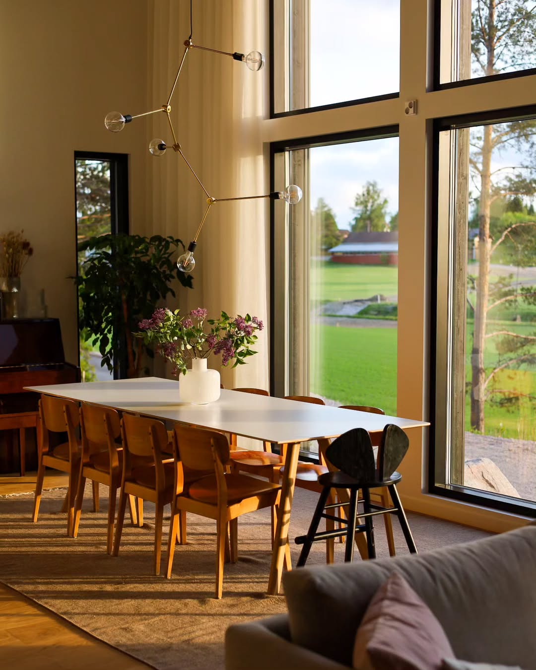 Dining room with large windows, table, chairs, and a view of greenery outside.