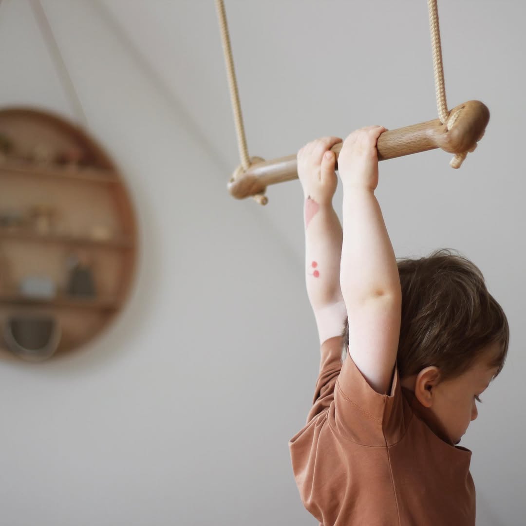 Child hanging from a wooden bar on a rope, with a neutral background