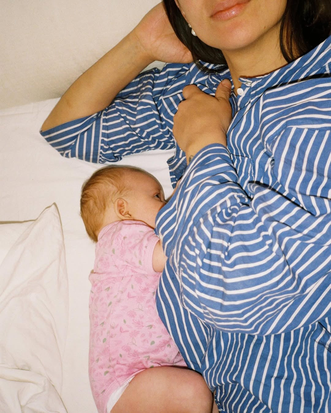 Woman in a blue and white striped shirt holding a baby in a pink outfit.