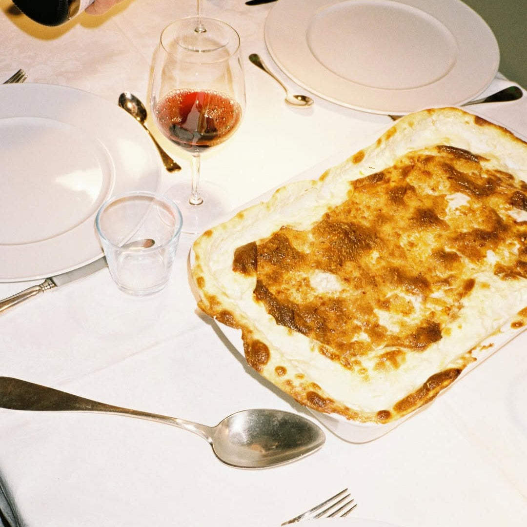 Dinner table with a pizza, wine glasses, and cutlery on a white tablecloth.