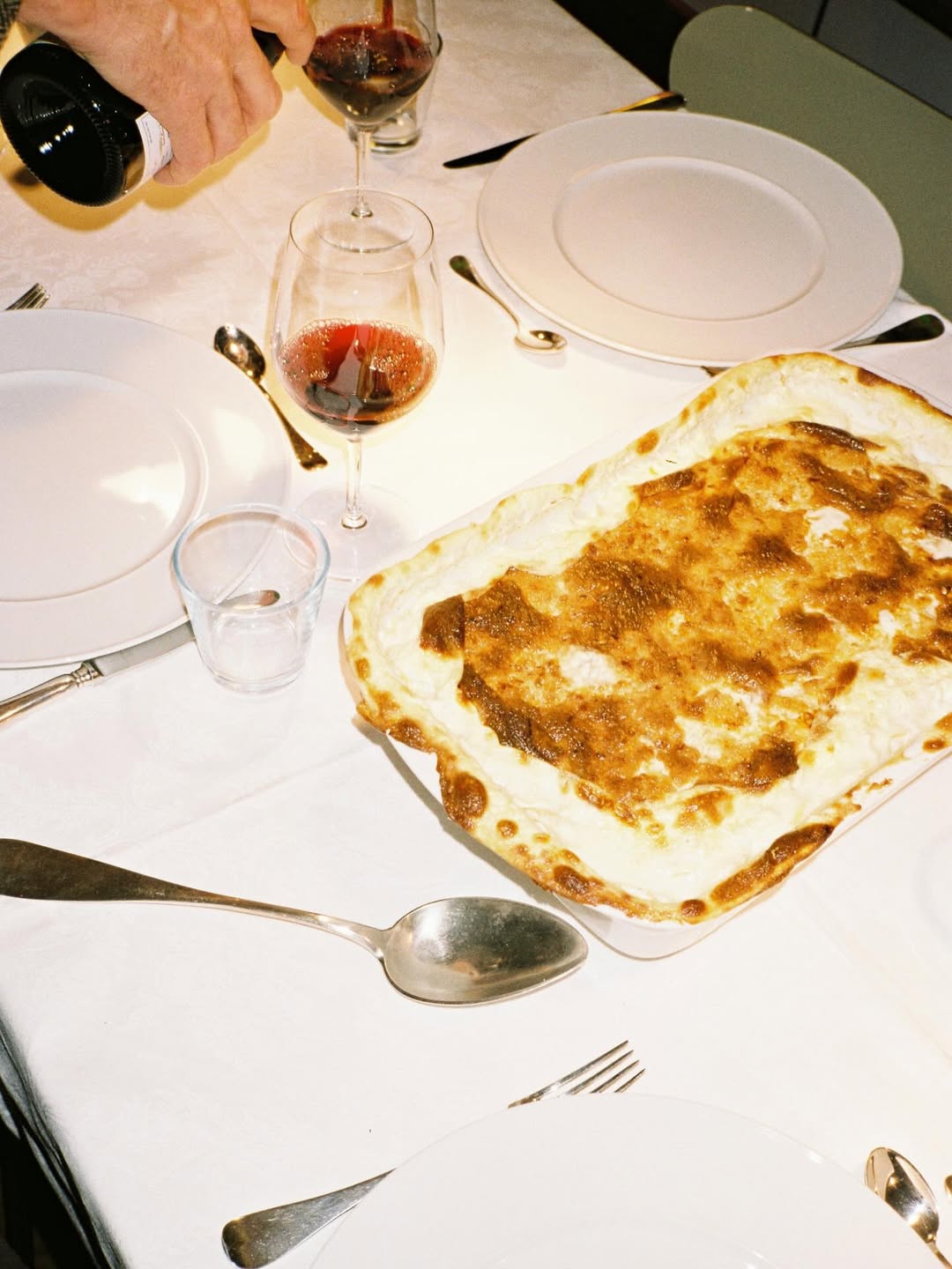 Dinner table with a pizza, wine glasses, and cutlery on a white tablecloth.
