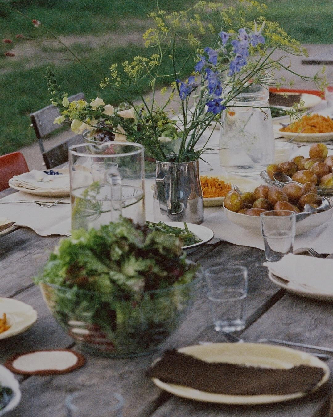 Dining table set with plates, glasses, and a floral centerpiece outdoors.