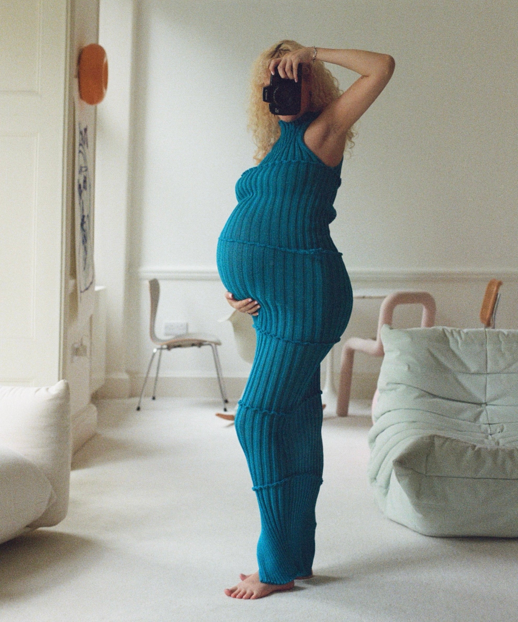 Person wearing a blue knit outfit taking a mirror selfie in a minimalistic room.