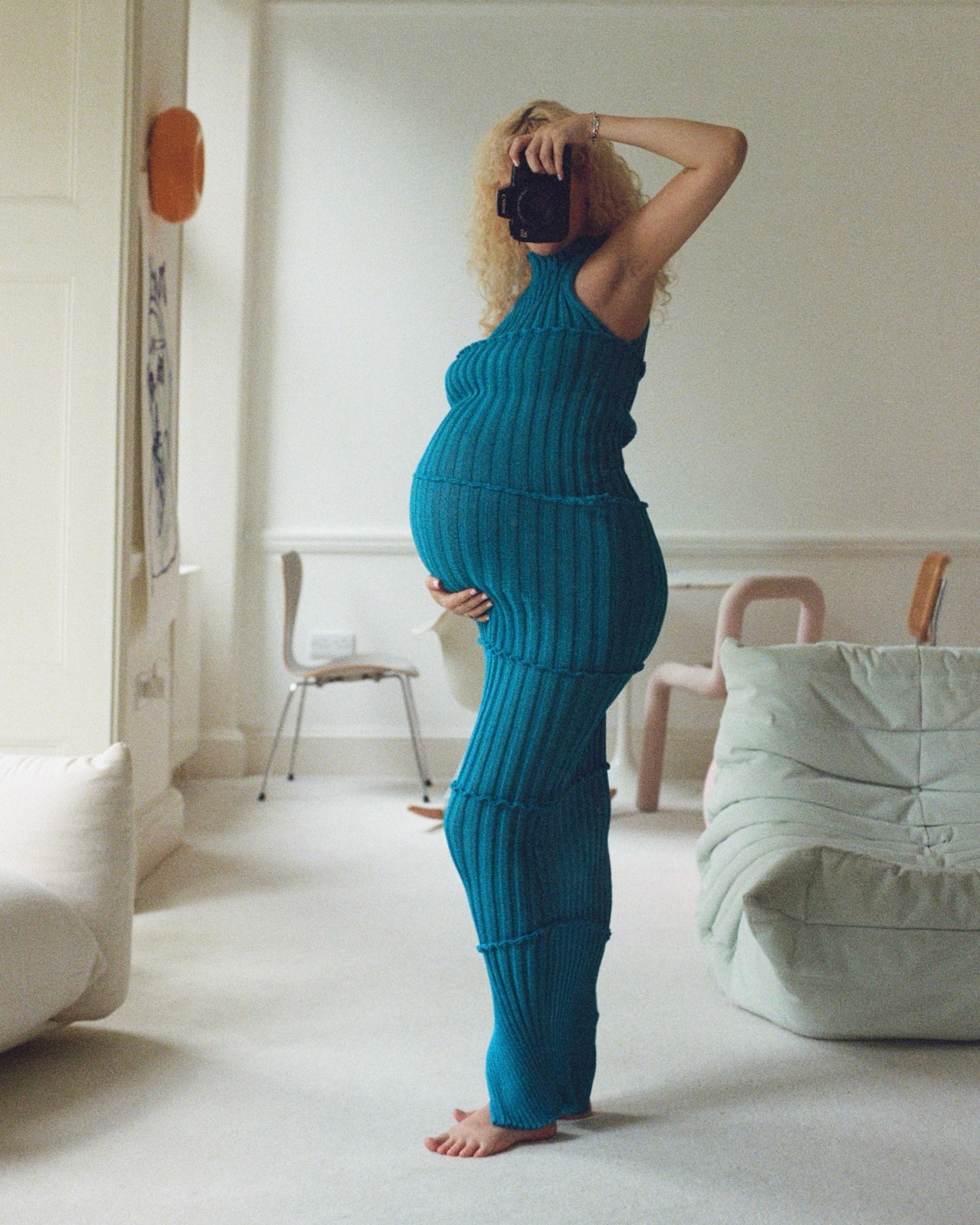 Person wearing a blue knit outfit taking a mirror selfie in a minimalistic room.