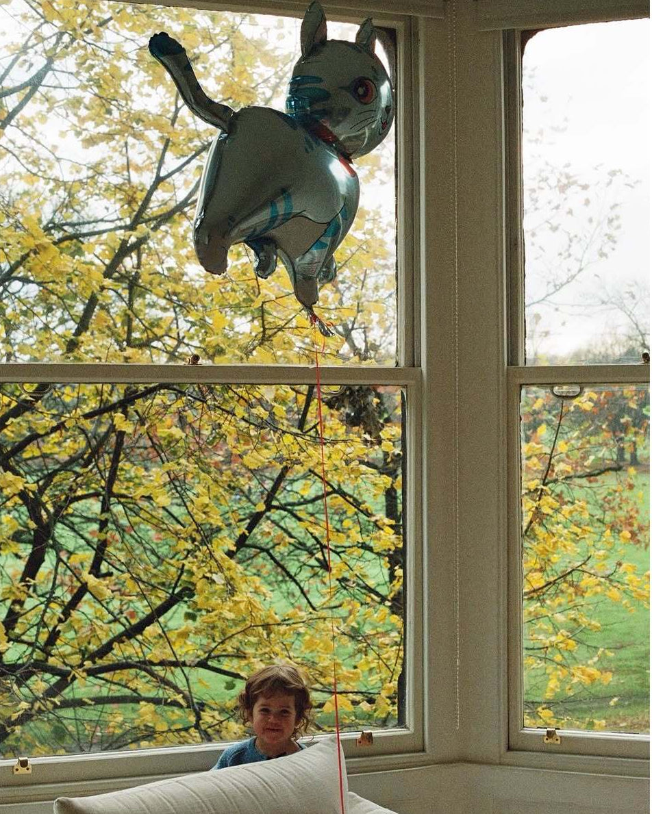 Child looking out a window with a decorative cat figure hanging from the frame.
