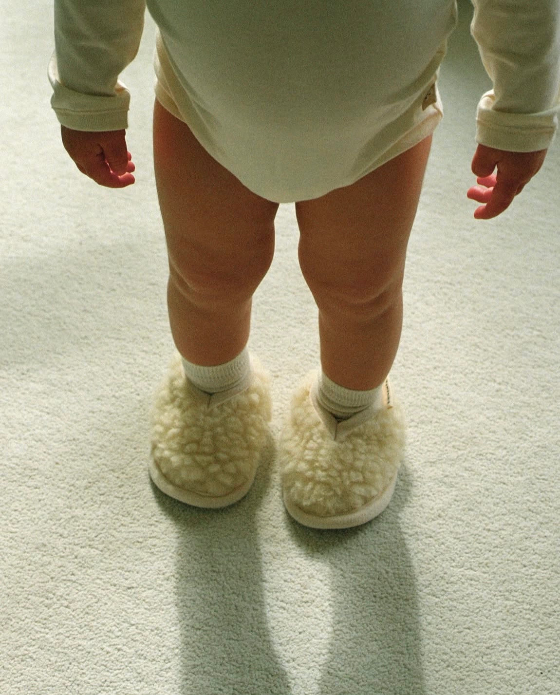 Child wearing white fluffy slippers on a light carpet