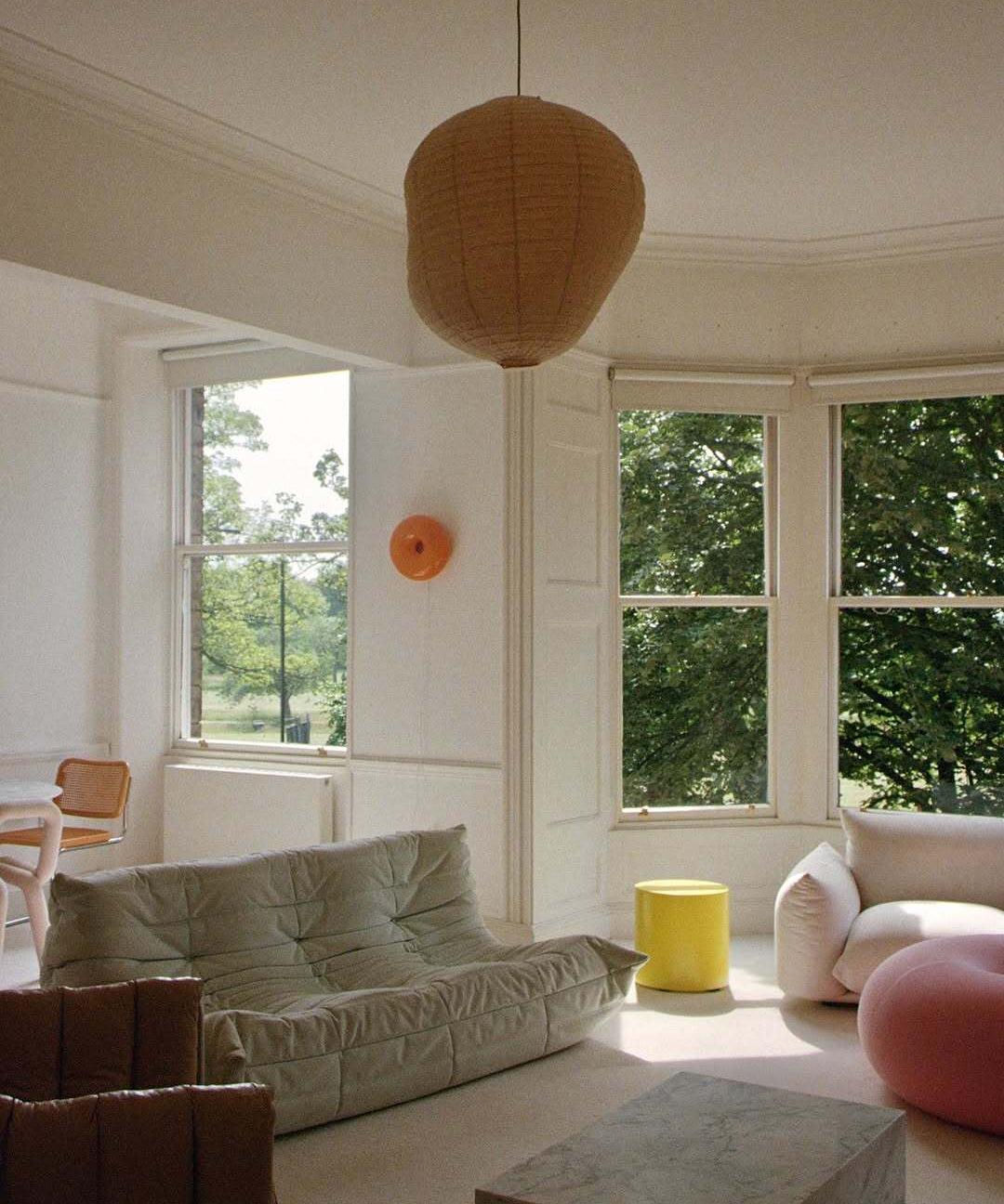 Modern living room with a beige sofa, yellow stool, and large windows.