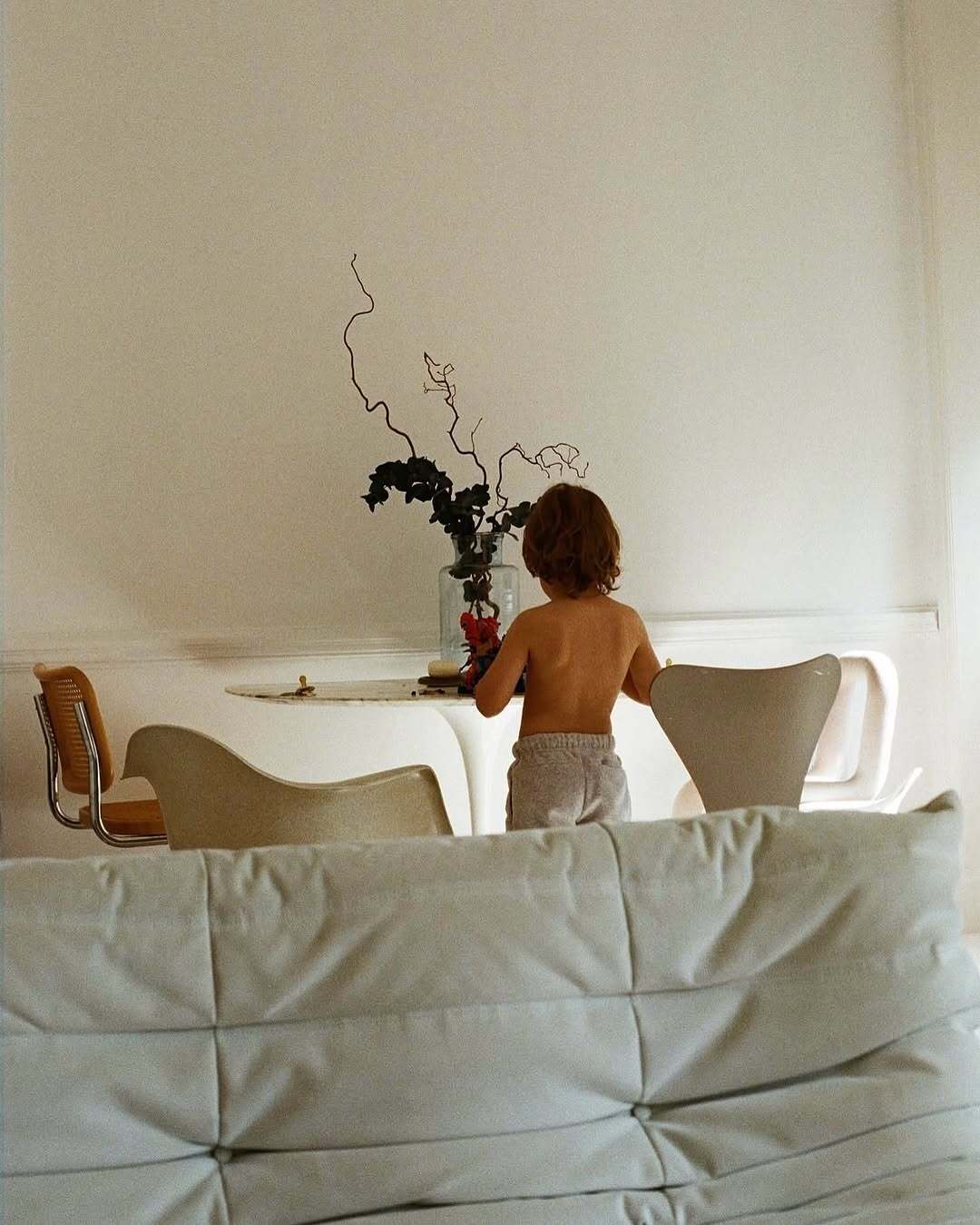 Person standing in a minimalistic room with a vase of flowers on a table.