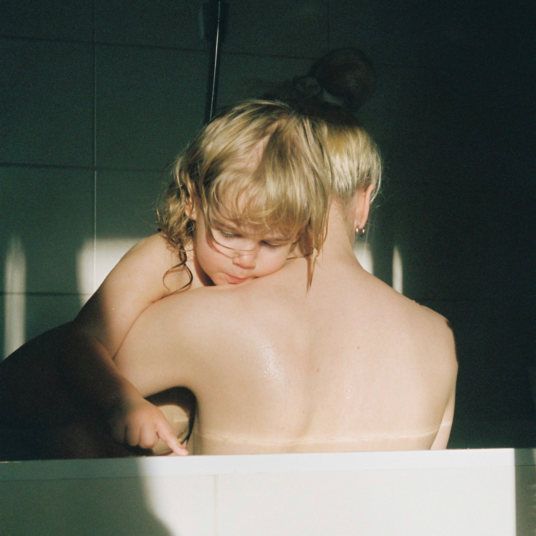 Two children in a bathtub with sunlight streaming in, creating a warm and intimate atmosphere.