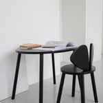A minimalist black oval desk paired with a matching black chair in a bright, modern room with white walls and a gray floor.